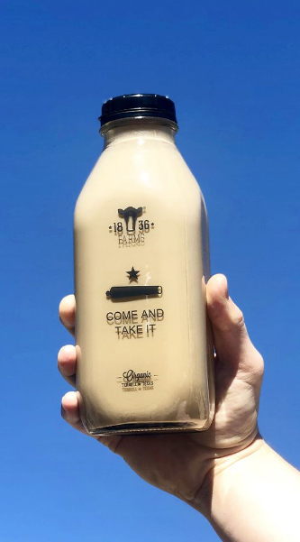Hand holding 1836 Farms "Come And Take It" Bottle backdropped by the blue sky